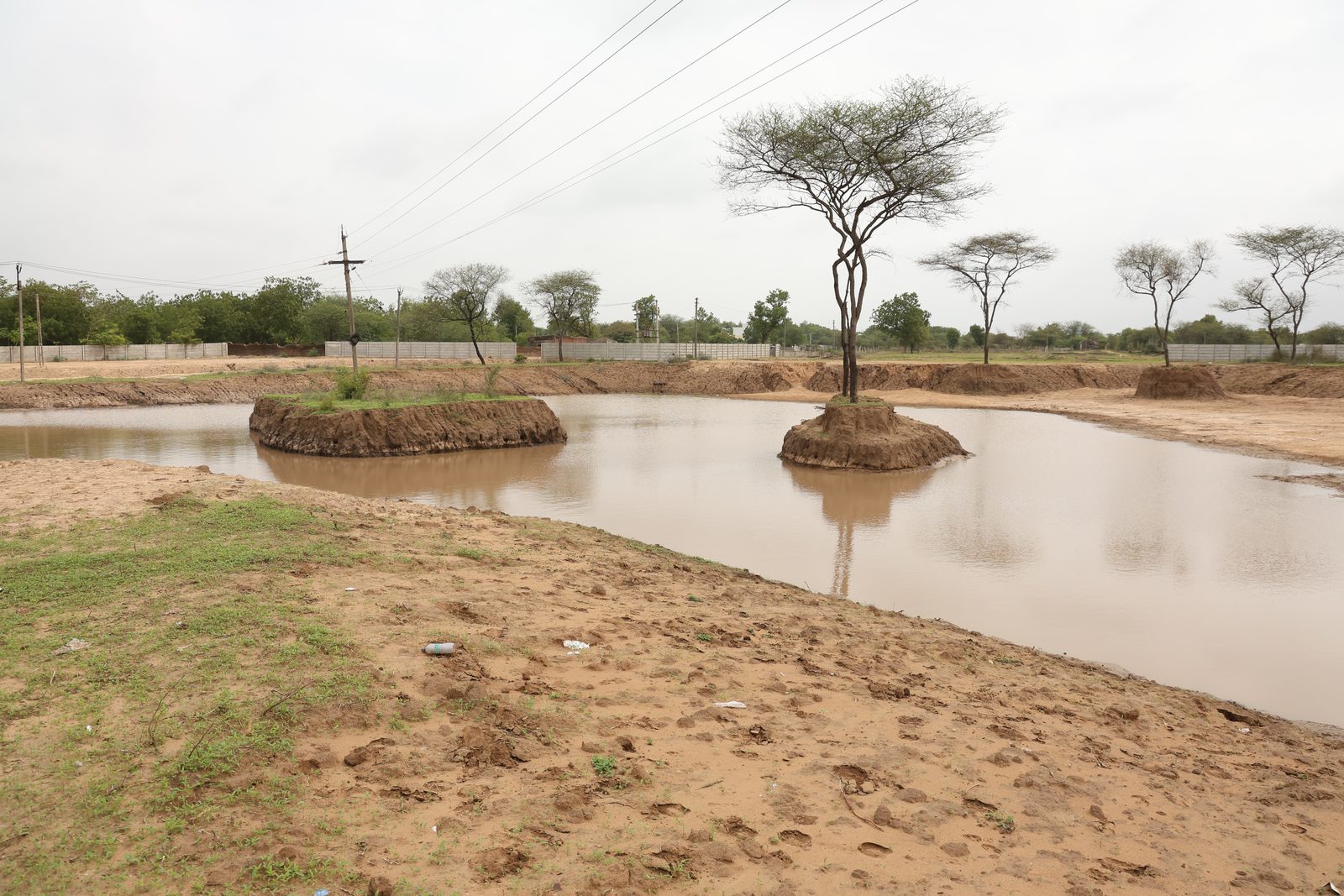 The excavated rainwater lake at Lapkaman holding water, with a central island and native trees